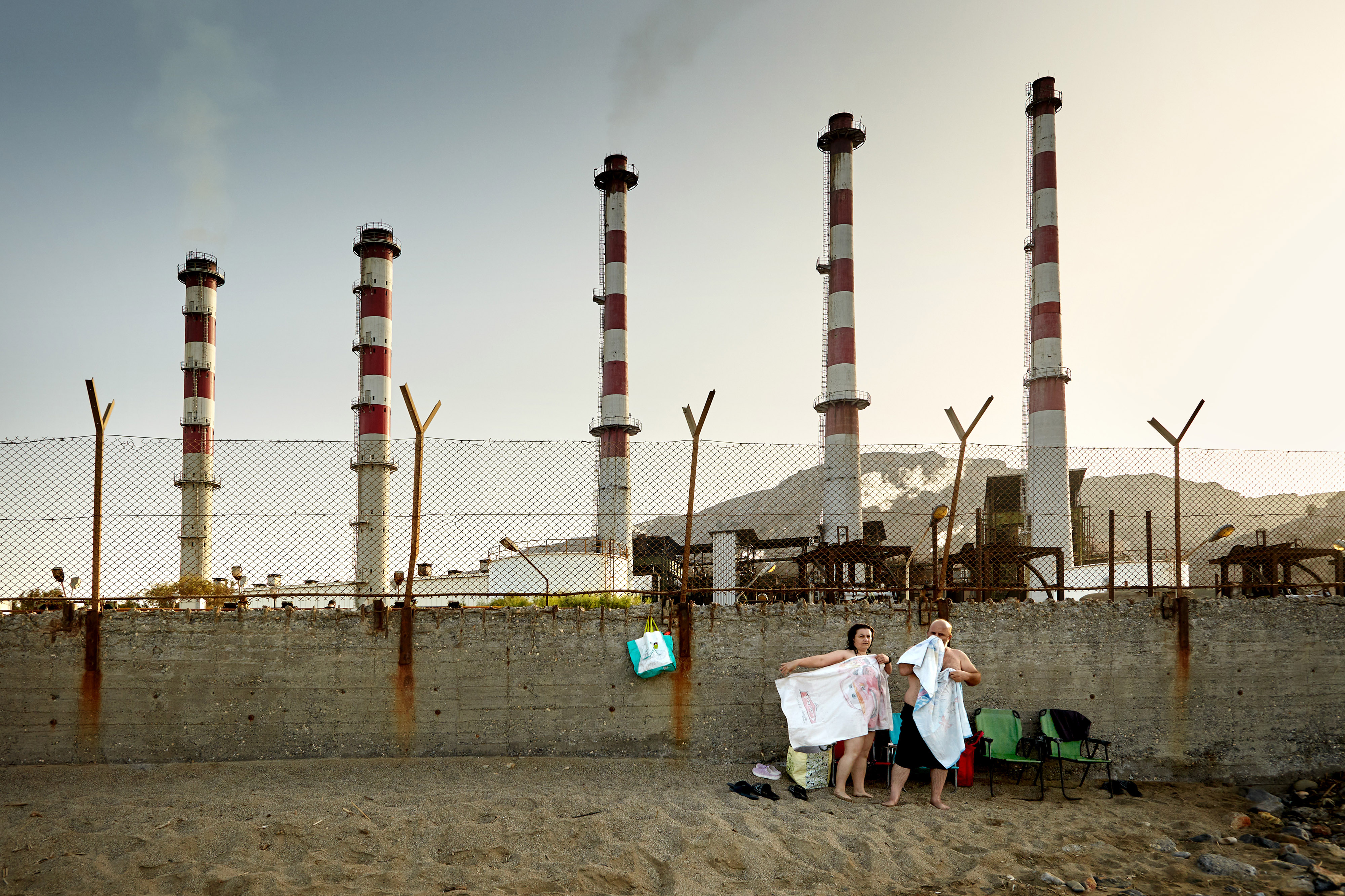 The photo was taken in Greece. A huge factory broke into the sea, taking the beach away from restful people. A simple, ordinary scene is very symbolic for me.