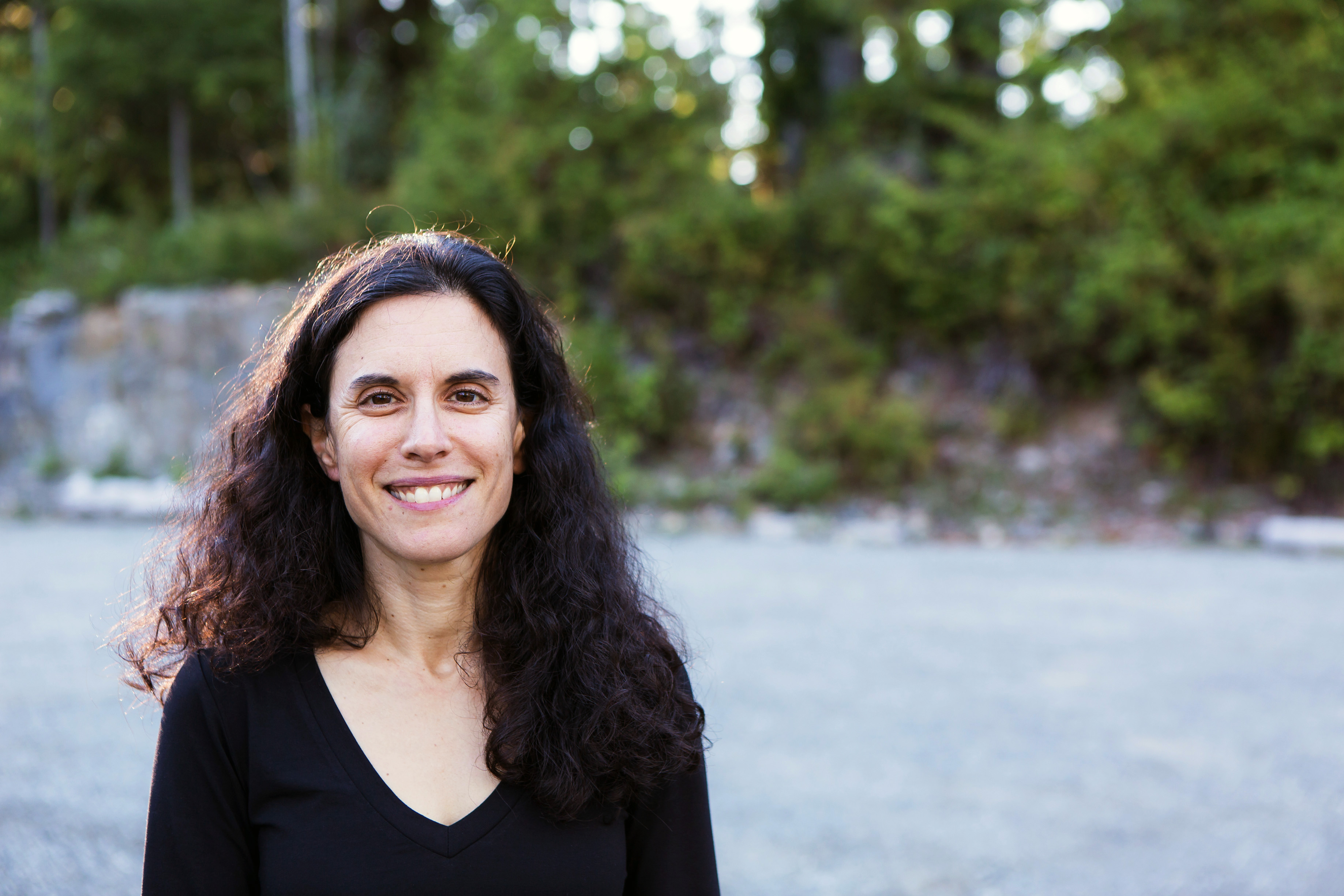 outdoor headshot of a smiling woman with long, dark, curly hair