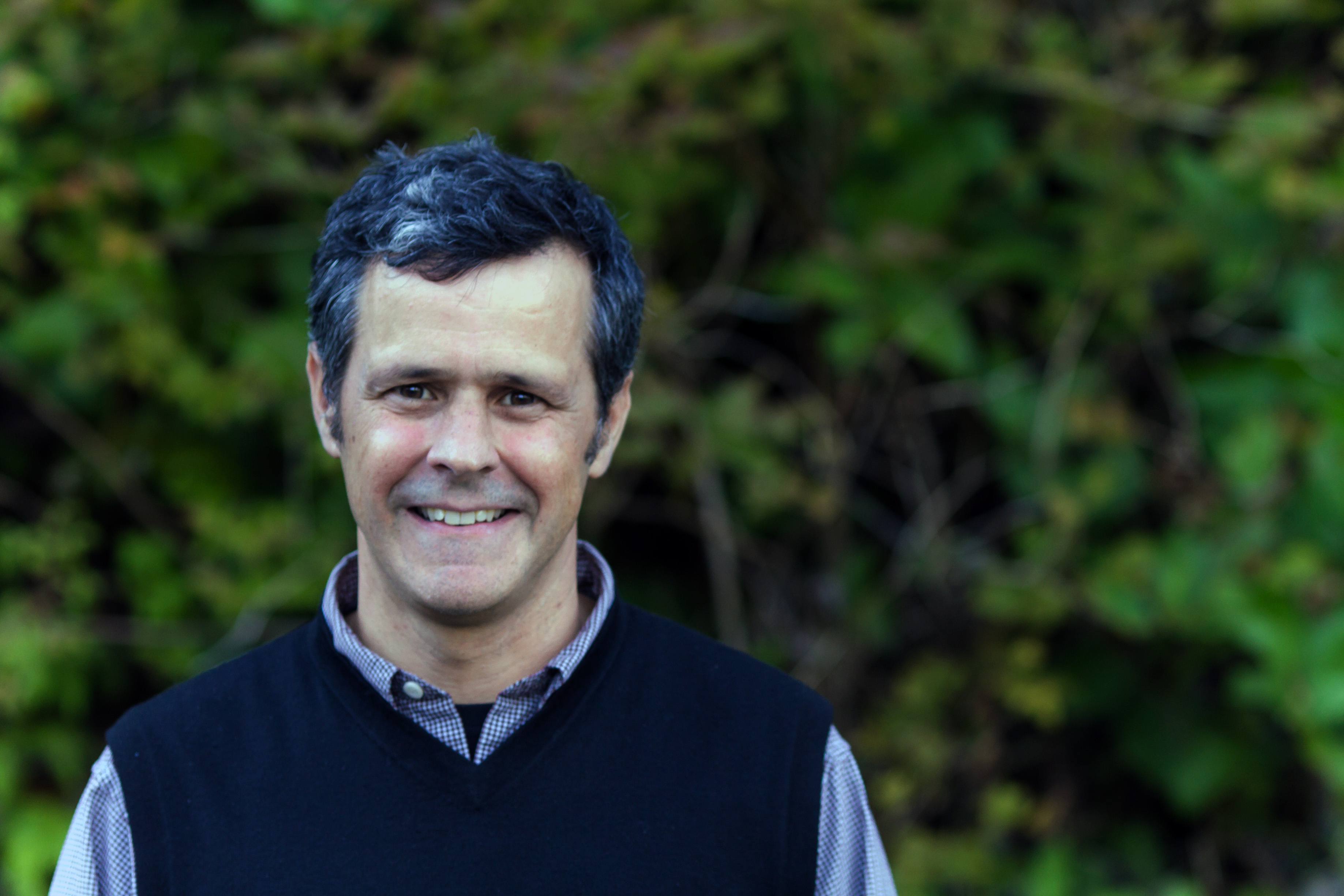 outdoor headshot of a smiling man with dark hair